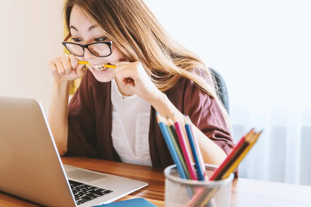 A stressed woman biting a pencil while working on her laptop.