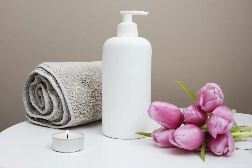 Spa essentials, including a rolled towel, lotion bottle, lit candle, and fresh pink tulips, set the scene for a relaxing aromatherapy massage.