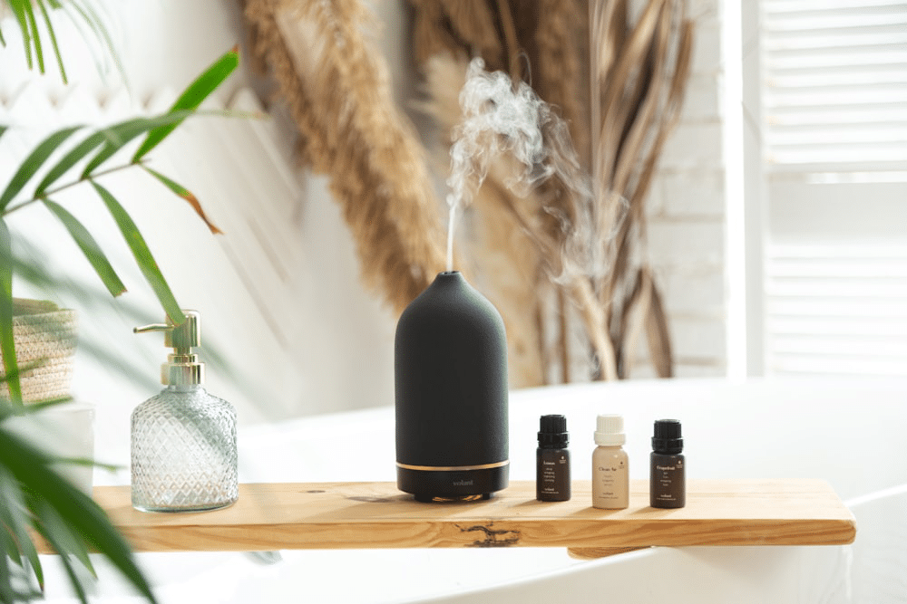 An essential oil diffuser releasing a calming mist next to aromatherapy oils and a glass soap dispenser on a wooden shelf in a serene spa setting.