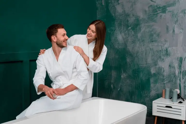 A smiling couple in white robes engaging in a playful moment before spa treatment, reflecting a shared wellness experience.