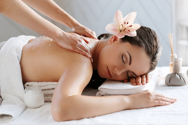 a massage therapist massaging the shoulders of a woman lying on a massage table with a flower in her hair