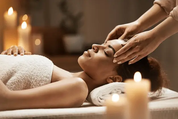 a massage therapist massaging the temples of a woman lying on a massage table
