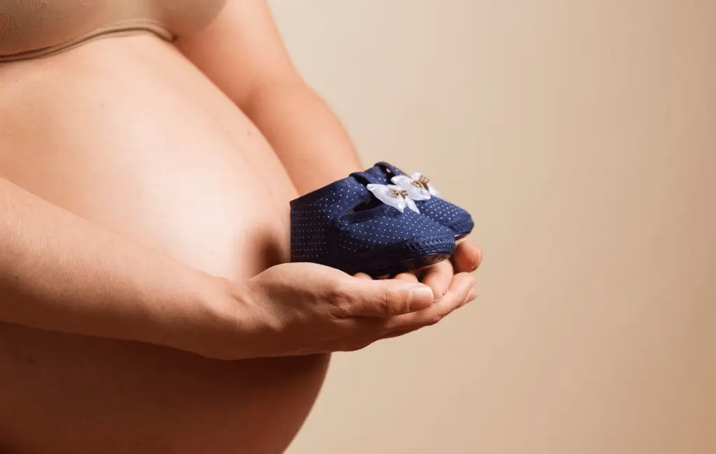 A pregnant woman holding baby shoes