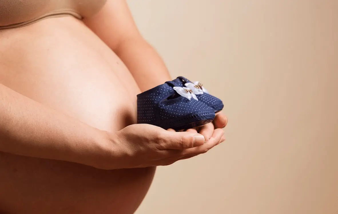 A pregnant woman holding baby shoes