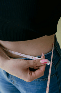 A woman measuring her waistline after getting non-invasive body contouring.